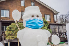 冬日仙境，雪地公园里，一个戴着医疗面罩，笑容满面的雪人。问候语或节日文稿的空白复制空间