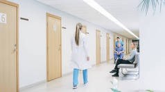 在医院的走廊里，忙碌的专业人员走过，护士推着轮椅上的老人，病人在等医生。全新医院，配备专业医护人员.