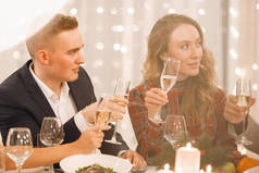 一对年轻夫妇坐在节日桌上，喝着香槟酒，面带微笑，在餐馆里聊天。有选择的焦点，模糊的灯光.