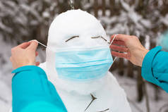 戴着医疗面罩的雪人- -一种新的现实，一种对疾病、感染、兽疫流行中的生命的保护。女人的手戴着雪人面具。冬季家庭户外活动