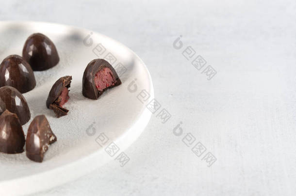 白盘上的自制黑巧克力糖果.覆盆子里塞满了糖果一块糖切成两半.