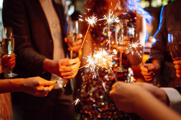 手里拿着闪闪发光的火花。一群快乐的人在聚会上手握火花.年轻的朋友们在<strong>夜总会</strong>里碰杯香槟.庆祝活动、人与假日概念.