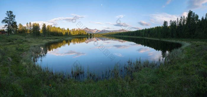 一座长满青草的高山湖上的全景。雪山、云和月亮在水中反射出来.夏夜，阿尔泰.