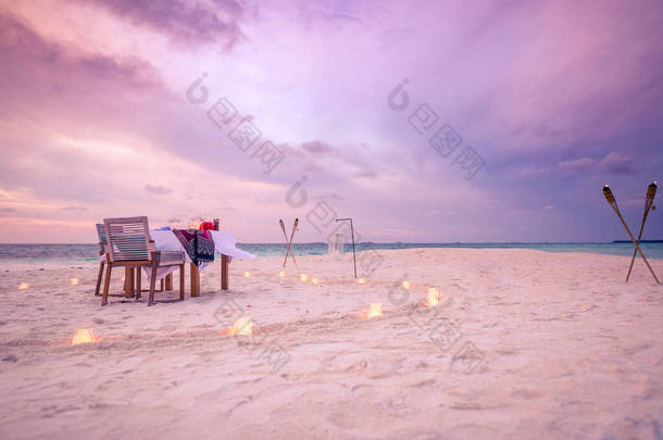 令人惊奇的浪漫晚餐在沙滩上的木制甲板与蜡烛下日落的天空。浪漫和爱情，奢华的目的地晚餐，异国情调的餐桌布置，海景尽收眼底