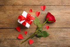 Beautiful gift box, paper hearts and rose on wooden table, flat lay. Valentine's Day celebration