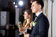 手拿着香槟酒的新婚夫妇听着祝酒词，恭贺客人