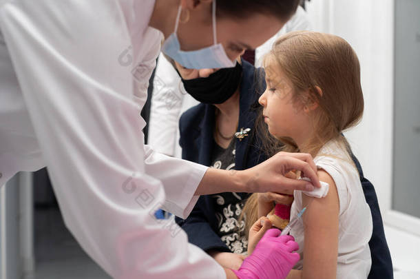 一名护士用新疫苗把针插在女孩的胳膊上。奶奶在接种疫苗的过程中为她孙女欢呼.医生给孩子的胳膊打必要的针.预防