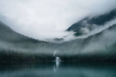 小溪在树间奔流，流入高山湖中。多雾的景色,高原湖,低云密林.浓雾中的针叶林高山大气景观.
