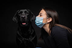一个拉布拉多猎犬的肖像，带着一个保护的医疗面具和一个女主人在一起。这张照片是在摄影棚拍的