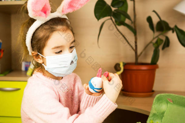 兔子耳朵里的一个女孩用鸡蛋和塑料做成了一个戴着医疗面罩的复活节兔子。DIY sitting at home, preparing for a religious holiday, home inter