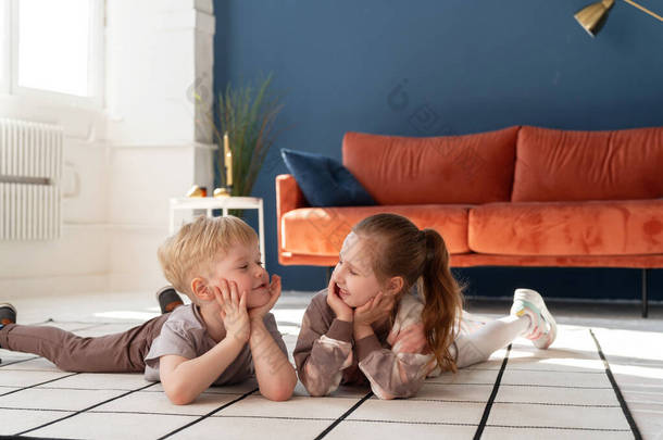 快乐的白人小孩，男孩和5岁的女孩，穿着舒适的衣服，躺在地板上，看着彼此交流。快乐的童年B.广告