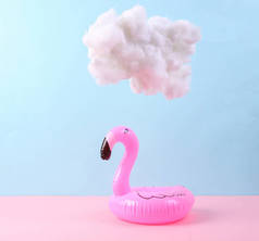 粉红蓝底上有云彩的可充气火烈鸟。创意。夏天快乐。最小的概念。色彩斑斓