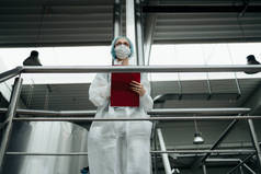 在医疗用品研究和生产工厂工作的从事保护工作的女工。她站在控制桥上，看着生产线。检查质量控制.
