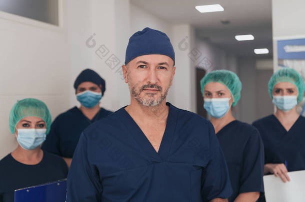 在covid-19爆发期间，整形外科医生在他的多族裔医疗团队面前戴着口罩。外科医生在他的同事面前。有选择的重点.