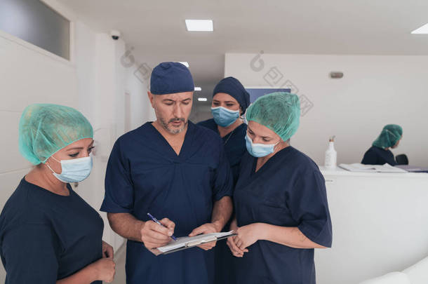 在covid-19爆发期间，整形外科医生在他的多族裔医疗团队面前戴着口罩。外科医生在他的同事面前。有选择的重点.