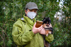 在COVID-19森林里，一个戴着口罩和带着狗散步的女孩在用智能手机拨号.