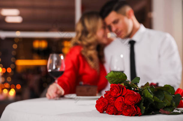 可爱的情侣们在餐厅庆祝情人节，聚精会神地围坐在红玫瑰桌旁