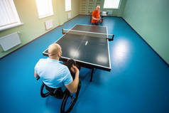 坐在轮椅上的成年残疾人和他的教练一起打乒乓球