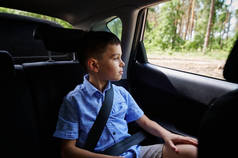 惊慌失措的少年坐在安全车的助推器座椅上，开车时从窗户往外看