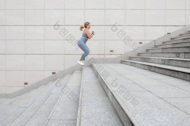 超大年轻女子在户外跳上楼梯，跑前热身的侧视图