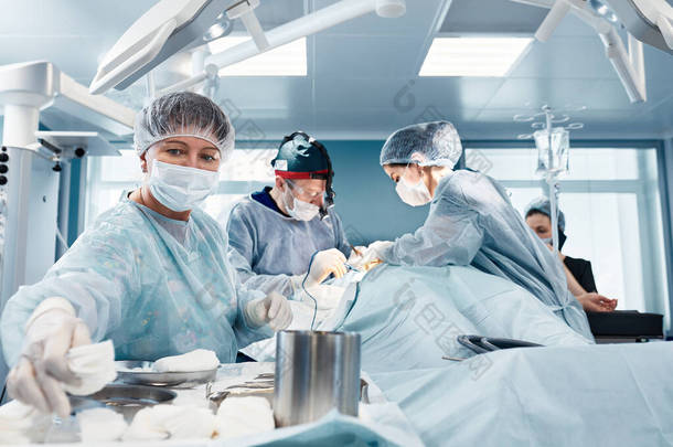在一个真正的手术中，一位女外科医生在一个现代手术室的一组外科医生的帮助下，在整形手术中提供了一些器械，从而挽救了生命.