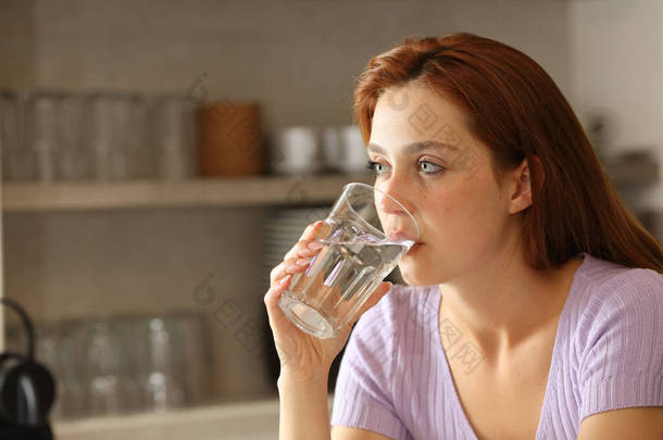 一个严肃的女人在厨房里用玻璃杯喝水