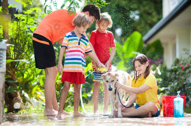 孩子们在夏天的花园里洗狗.<strong>水</strong>管和洒<strong>水</strong>的乐趣为孩子。百花盛开的后院,孩子们在户外的庭院里洗小狗.孩子们玩。带着宠物的孩子家庭<strong>浴</strong>犬。动物护理.