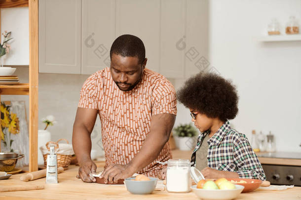 可爱的小男孩看着他的父亲把面团做成烘培的样子