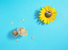 太阳是由有眼睛、阳伞、贝壳和海星的葵花子制成，躺在淡蓝色的背景上。简约创意海滩概念，平铺构图