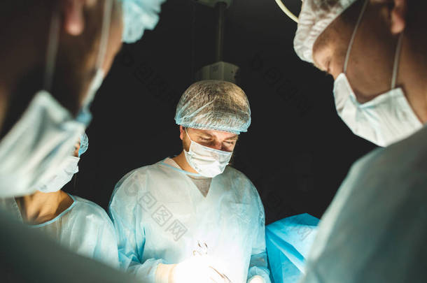 一个由外科医生、助理和麻醉师组成的国际专业小组对全麻病人进行复杂的手术。低调的黑暗大气<strong>摄影主题</strong>.