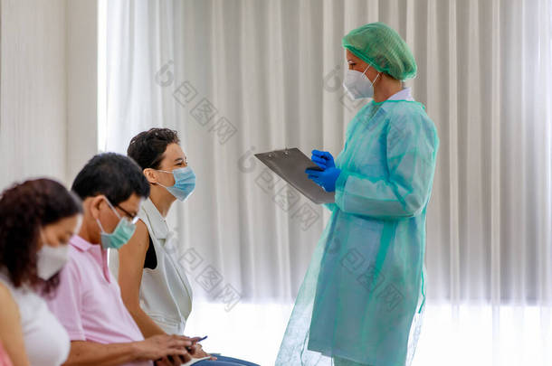 年轻<strong>的</strong>女公民戴着口罩，站在科罗纳威斯疫苗接种员队伍中，坐在旁边<strong>的全副武装的</strong>护士手中，从纸板上查看她<strong>的</strong>个人信息.
