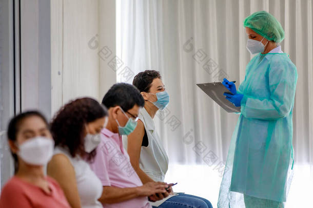 年轻的女公民戴着口罩，站在科罗纳威斯疫苗接种员队伍中，坐在旁边的全副武装的护士手中，从纸板上查看她的个人信息.