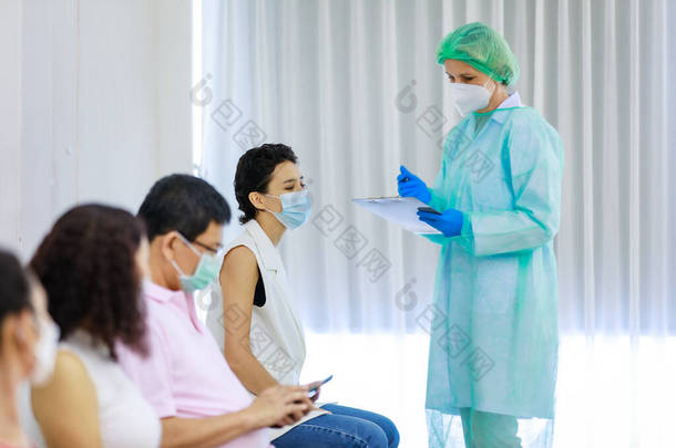 <strong>年</strong>轻的女公民戴着<strong>口罩</strong>，站在科罗纳威斯疫苗接种员队伍中，坐在旁边的全副武装的护士手中，从纸板上查看她的个人信息.