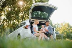 有三个身穿白衣的年轻人在野餐.美丽的父母和女儿在暑假期间开车旅行.