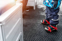 在溜冰场更衣室里，穿着蓝色塑料租借溜冰鞋站在防滑橡胶软垫上的小孩腿的特写画面。健康儿童康乐活动