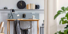 斯堪的纳维亚家庭办公室内，配有木制书桌、设计椅、带有架子的木镶板、植物、台灯、地毯、办公用品和雅致的现代家居装饰配件.