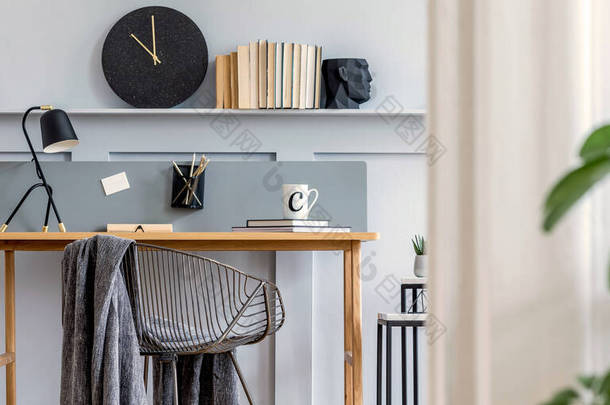 斯堪的纳维亚家庭办公室内，配有木制书桌、设计椅、带有架子的木镶板、植物、台灯、地毯、办公用品和雅致的现代家居装饰配件.