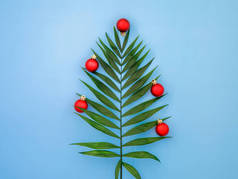 具有创意的圣诞树，由棕榈叶和红球做成，背景是现代蓝皮书热带新年假期的海上、旅游、游轮、航行理念。平面放置顶视图，复制空间