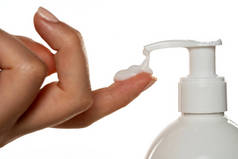 一瓶装有水泵的化妆品把奶油倒在一个女人的手指上，涂在一个白色的背景上