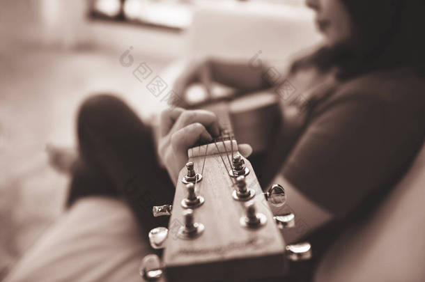 女人坐在沙发上，弹吉他放松身心，给人留下模糊的印象，用音乐来放松身心.