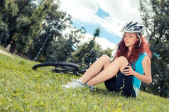 美丽的红发女孩骑马和骑自行车在城市公园中的一辆自行车
