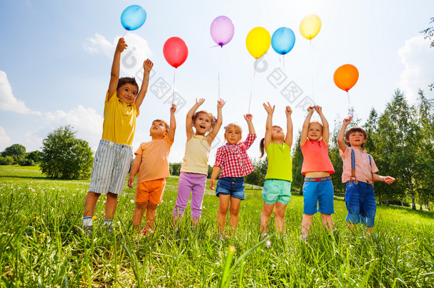 用气球和双臂高举在天空中的快乐的孩子