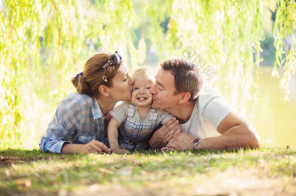 快乐的父母亲吻蹒跚学步的男孩。父亲、 母亲和儿子躺在草坪上.