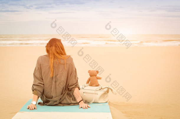 年轻单身女子，坐在海滩看海-虚构友谊与忧郁感觉孤独和寂寞概念 — — 温暖复古筛选器与增强阳光的泰迪熊