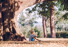 男孩拿着本书坐在大树下 
