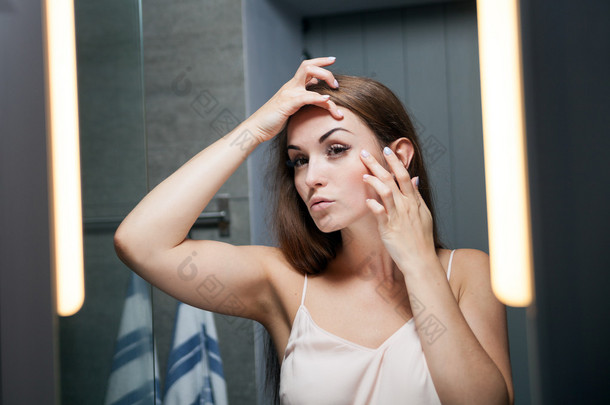 检查在浴室的镜子前脸上的皱纹的女人