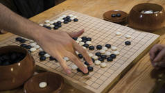 手在中国围棋或围棋游戏板上玩黑白石头。人工照明的室内活动.