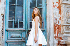 美丽的女孩在一条蓝色的门边的白色连衣裙