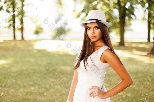 美丽的年轻女子，在白色的衣服，在帽子上一个夏日户外摆姿势