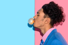 在粉红色和蓝色背景上的英俊男子吹口香糖关闭